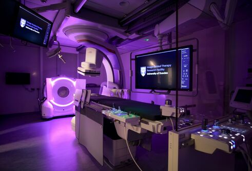 A room featuring a large screen mounted on the wall and medical imaging equipment in the foreground