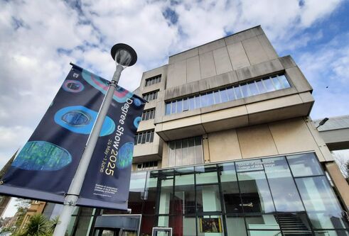 Image of advertising flags hanging from pole outside building, looking upwards at the flags and building