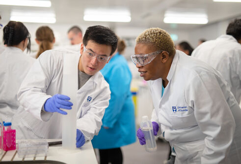 Two students with white lab coats on conducting an experiment in a lab at Dundee