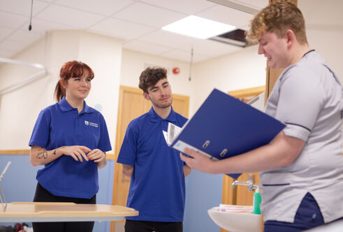Nurse standing with a clipboard talking to Dundee nursing students at the Clinical Skills Centre