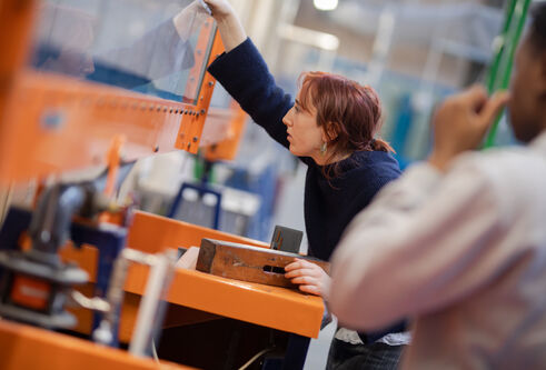A person leans over a large orange frame, looking through a clear piece of glass.