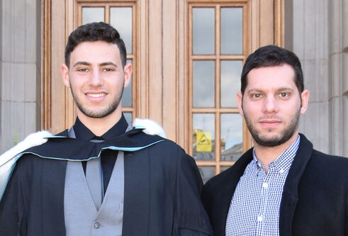 two men standing together, one in graduation gown