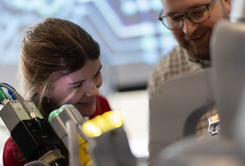 Two people are looking down and smiling at some apparatus 