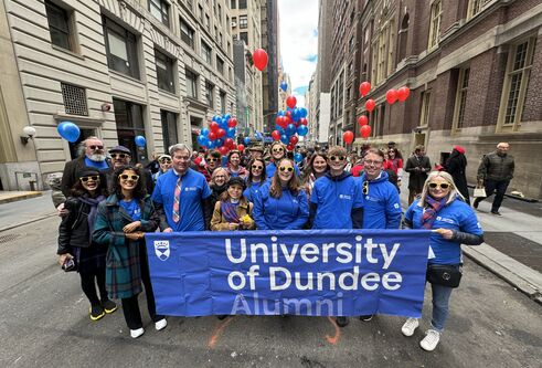 A group of people, standing behind a blue banner that reads University of Dundee pose for a photo