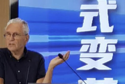 A man stood at a lectern in front of a screen featuring chinese writing