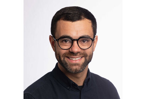 A head and shoulders photo of a man with short brown hair, beard and glasses smiling
