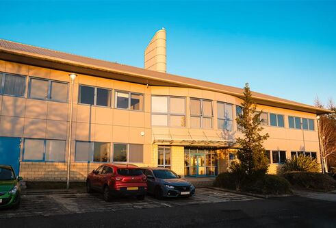 A brown building with lots of windows and two cars parked outside on a blue sky day.