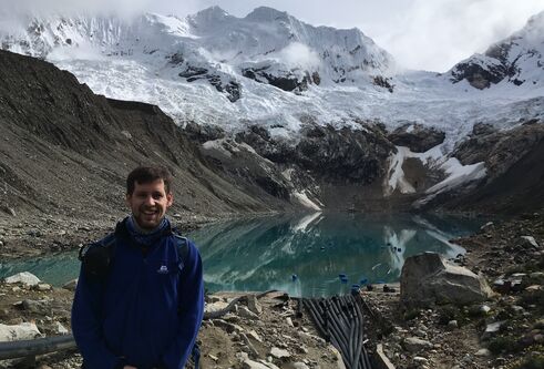 Man standing at the top of a mountain, with a pool of glacier water behind him