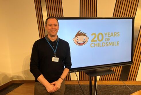 Keith Milburn stands next to the Childsmile logo