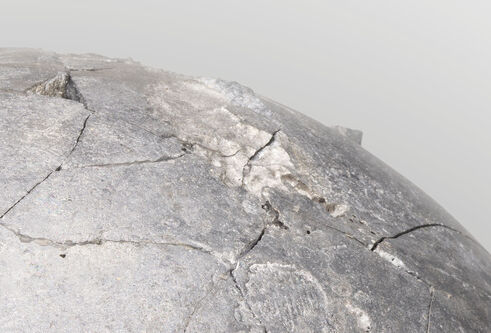 A section of a grey concrete looking sphere, against a pale grey background.