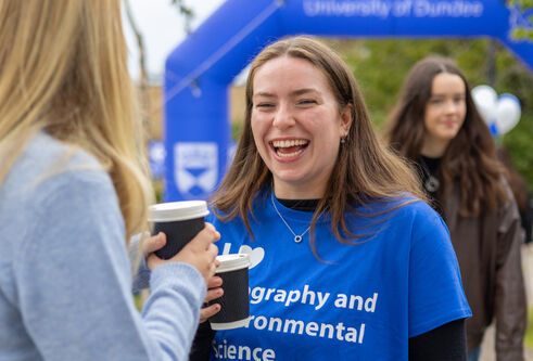 student in blue dundee uni top sharing coffee with friend