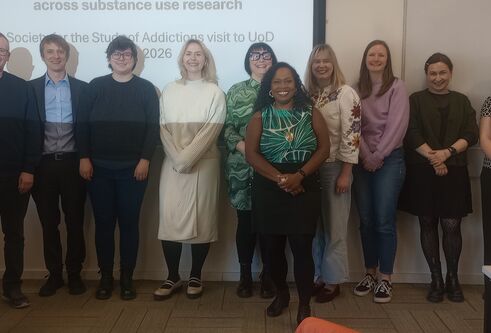 A group of people stand in front of a wide screen with the text Substance Use Research Group (SURG) in Health Sciences 