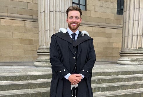 Adam Hall in graduation robes on the steps of the Caird Hall
