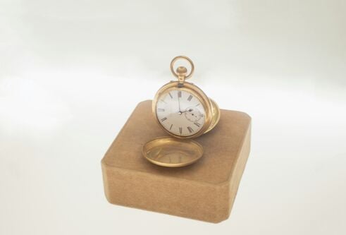 A gold pocket watch on a plinth against a white backdrop