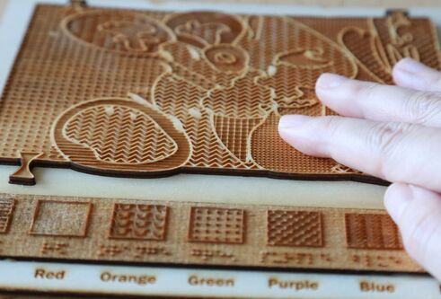 A hand touches a 3D model with raised elements designed to depict the visual appearance and colours of an artwork