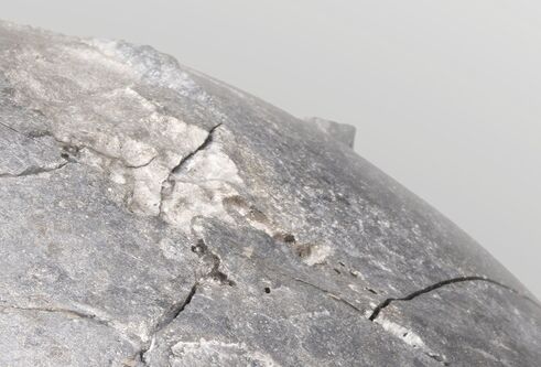 close up of a piece of artwork which is a dry crusty surface of a clay sphere, painted in a metallic silver colour