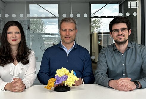 Co-corresponding author Alessio Ciulli (centre) and co-first authors Valentina Spiteri (left) and Alejandro Correa-Sáez (right) sat in front of a coloured model of the cryo-EM structure of the complex between the SMARCA2 bromodomain ( shown in orange), DCAF16 (purple), DDB1(ΔBPB) (yellow), and DDA1 (blue), glued by the degrader compound (grey)