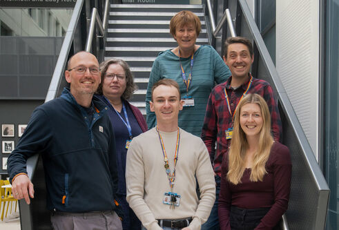 Six people stood together smiling while stood on a staircase