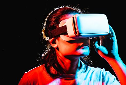 Person wearing a virtual reality headset illuminated by blue and red neon lighting against a dark background