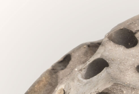 A section of a grey concrete looking sphere, with large holes, against a pale grey background.