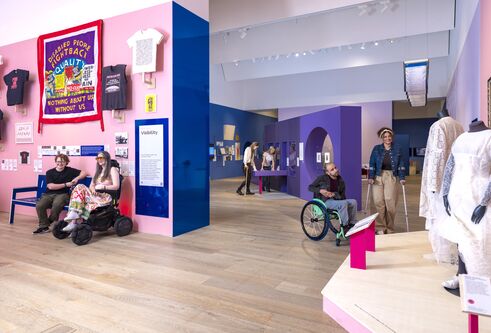 A iew of the exhibiton, with pink and purple-coloured rooms. Viewing the exhibits are people in wheelchairs and walking on crutches.
