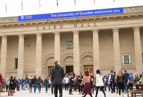 An exterior view of the Caird Hall on a sunny day, with graduates in the city square.