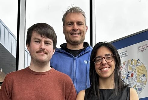 A line-up of researchers Connor Craigon, in orange t-shirt, Professor Alessio Ciulli in a blue sweater, and Maria Rodriguez-Rios, in a black top, and wearing round glasses.