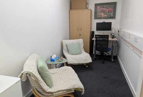 Two chairs with cushions covered with blankets with a computer, desk and office chair situated in a quiet room 