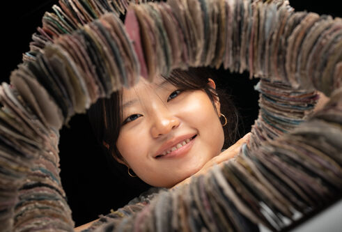 A headshot of Nayoung, smiling, whilst looking through a circle of her ceramic discs.