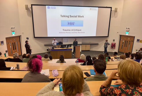 Large lecture theatre with attendees looking at a large screen for an event about Social Work