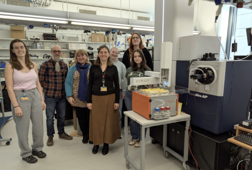 A group of staff stand together in a lab with several types of equipment around them