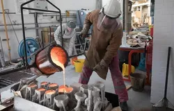 a person in protective gear pouring molten metal into moulds