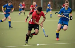 Person wearing red + black hockey kit holding a hockey stick, while competing in hockey match