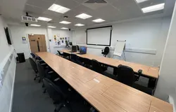 Dalhosuie 1LG02 showing two rows of desks and chairs. PCs are set inside the tables.  with a white screen on the wall