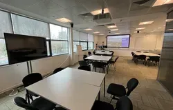 Dalhousie 1G10 - a room with several desks pushed together to form a square table with surrounding chairs and a tv screen and white screen at the far end