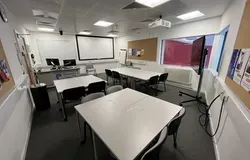 Dalhousie 2S11 - three sets of square tables with chairs, a mobile flat screen tv on the floor and a white screen on the far wall
