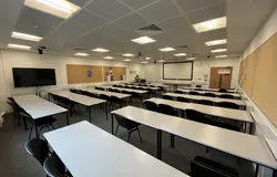 Dalhousie 2S13 - rows of tables and chairs with a white screen at the front of the room. A flat screen tv on a mobile stand on the floor 