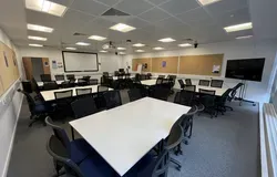 Dalhousie 2S14 - several tables set in squares with chairs. A mobile tv screen on the floor and white screen at front of room
