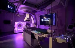  A room featuring a large screen mounted on the wall and medical imaging equipment in the foreground