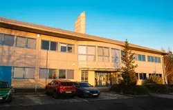 A brown building with lots of windows and two cars parked outside on a blue sky day.