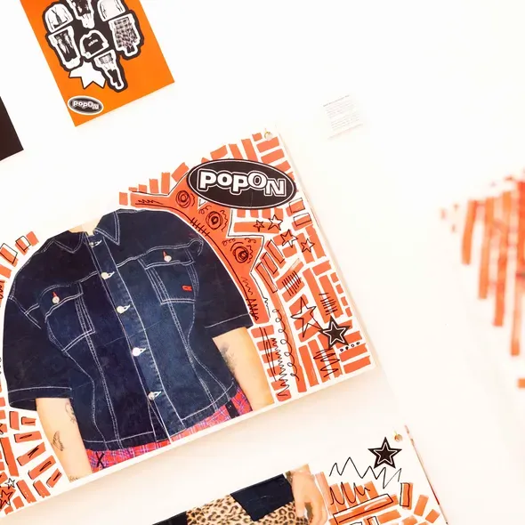 Graphic design posters in orange and white of mobile phones and a person in a denim jacket as part of the Degree Show 2025 exhibition
