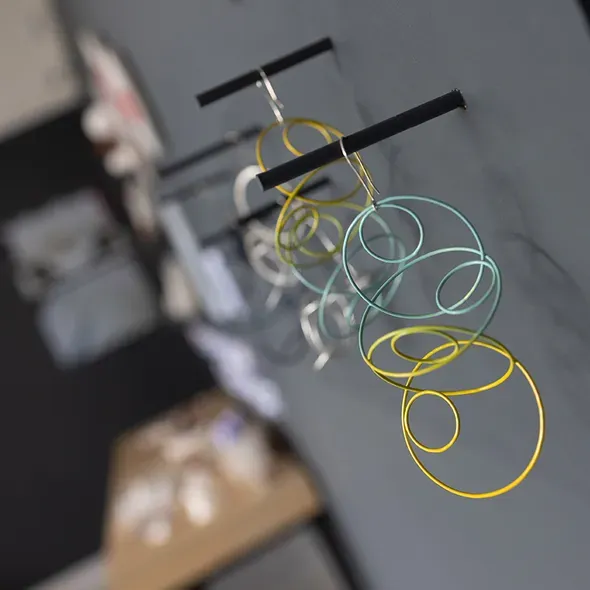 Close-up of colorful wire-loop jewelry pieces mounted on a dark wall at the graduate showcase 