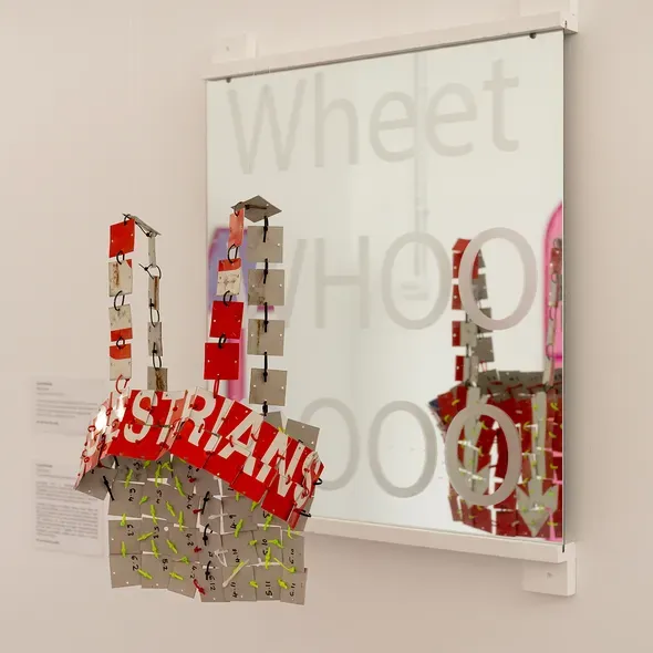 A red and white garment hanging from the ceiling in front of a mirror on the wall as part of the Master Show exhibition