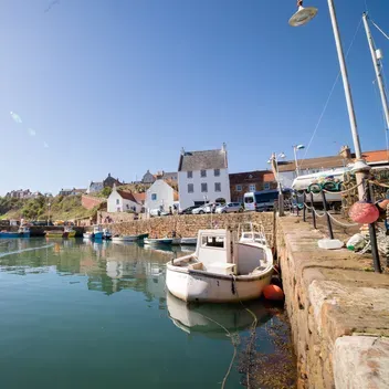 A small fishing boat comes into Crail Harbour, surrounded by buildings from the 17th-19th century