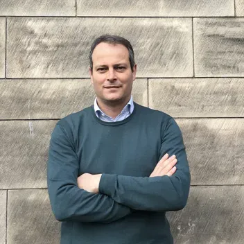 Portrait of Ernesto Bonafe standing against a wall with his arms crossed. 