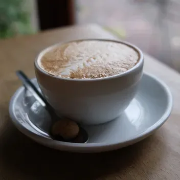 A photograph of a cup of coffee on a saucer with a teaspoon on a wooden table.