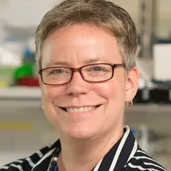 A woman with short hair and glasses, wearing a striped shirt.