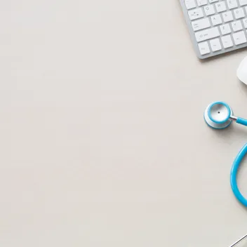 An aerial view of a desk with a stethoscope, mouse and keyboard on the right hand side