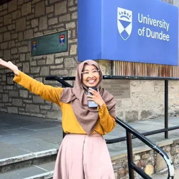 student standing on steps leading to a building with University of Dundee sign