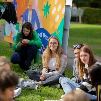 A cheerful group of young adults sitting on the grass, sharing laughter and stories in a vibrant outdoor environment.